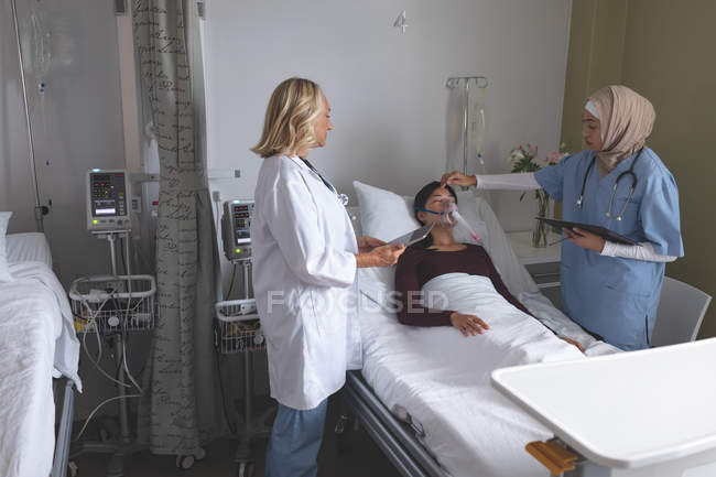 Vorderansicht diverser Ärztinnen bei der Untersuchung einer asiatischen Patientin auf der Station im Krankenhaus. — Stockfoto