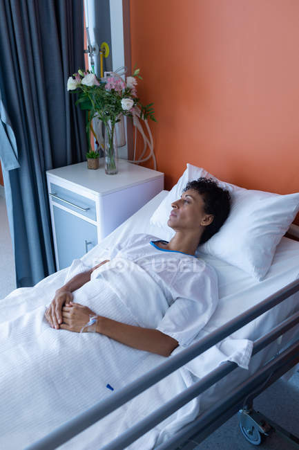 High angle view of middle aged mixed-race female patient sleeping in bed with hands on stomach in the ward at hospital — Stock Photo