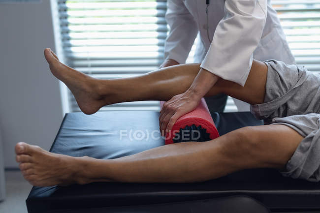 Side view of female doctor using foam roller on patient leg in hospital for physical therapy — Stock Photo