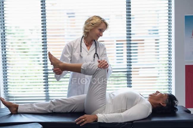 Vista frontal de la doctora caucásica examinando pierna de paciente mujer de raza mixta en el hospital - foto de stock