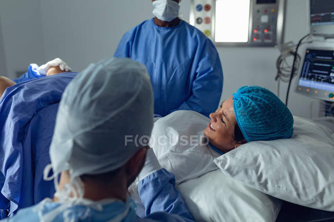 Visão lateral de diversos cirurgiões examinando a mulher grávida durante o parto, enquanto o homem segurando a mão na sala de cirurgia no hospital — Fotografia de Stock