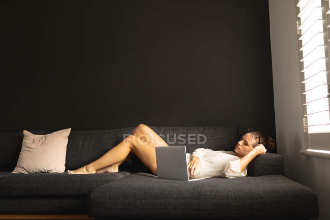 Вид збоку кавказька жінка з використанням ноутбука, відпочиваючи на дивані у вітальні вдома — стокове фото