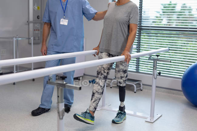 Низкая часть физиотерапевта-мужчины помогает пациенту ходить с параллельными решетками в больнице — стоковое фото