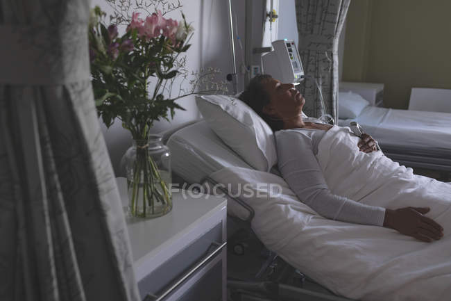 High angle view of beautiful mixed-race female patient sleeping in bed in the ward at hospital. Flowers are standing in vase on cupboard next to bed. — Stock Photo