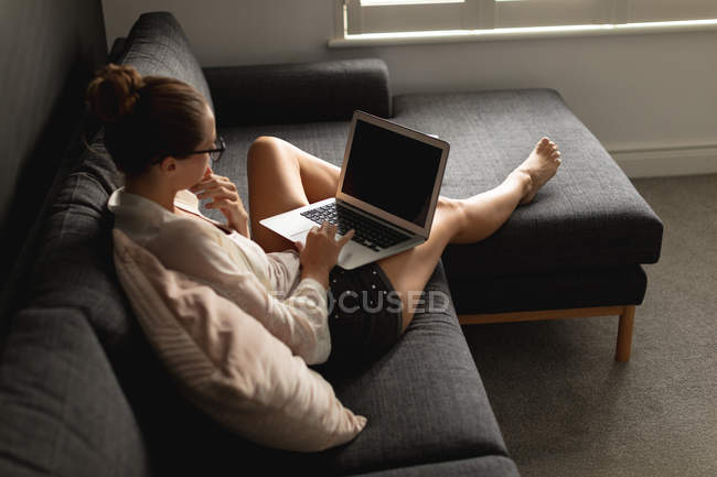 Vista alta de la mujer caucásica usando el ordenador portátil en un sofá en la sala de estar en casa - foto de stock