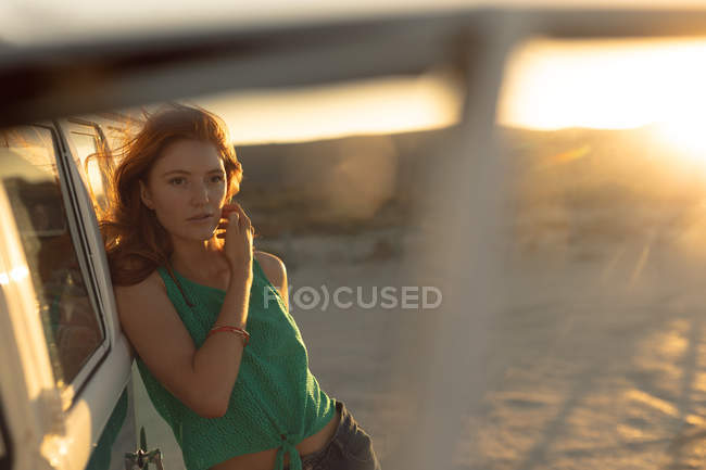 Vorderansicht der schönen jungen kaukasischen Frau, die sich am Strand auf einen Wohnwagen lehnt — Stockfoto