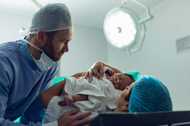 Vista lateral de pareja caucásica sosteniendo a su bebé recién nacido en quirófano en el hospital - foto de stock