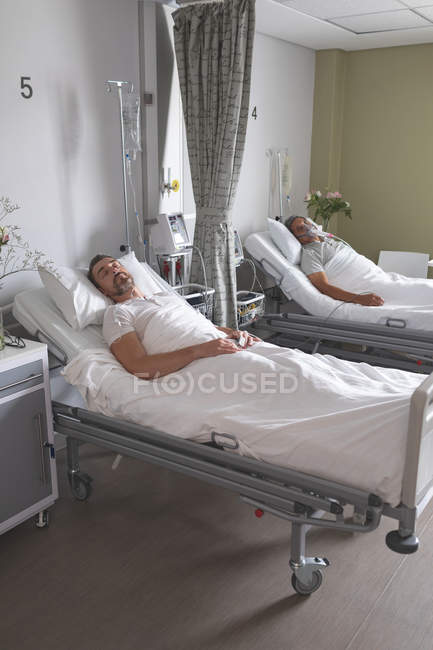 Vue latérale de patients masculins caucasiens dormant sur le lit dans la salle à l'hôpital — Photo de stock