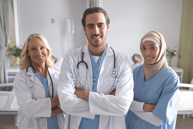 Vista frontal de diversos médicos de pie con los brazos cruzados en la sala en el hospital - foto de stock