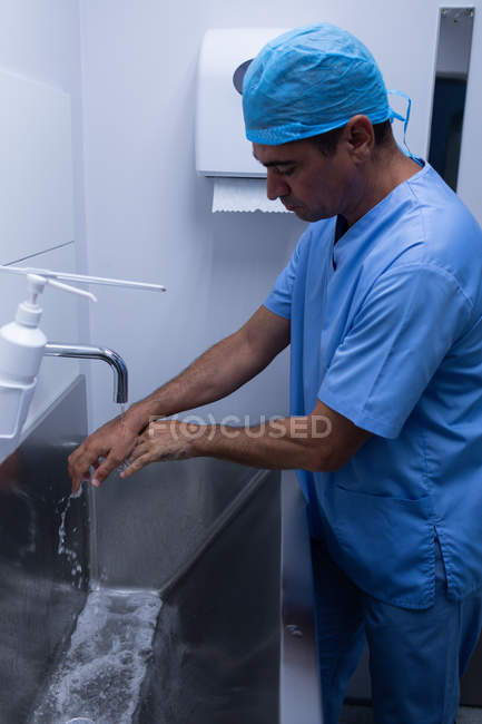 Seitenansicht eines hübschen kaukasischen Chirurgen, der sich im Krankenhaus im Waschbecken die Hände mit Seife wäscht — Stockfoto
