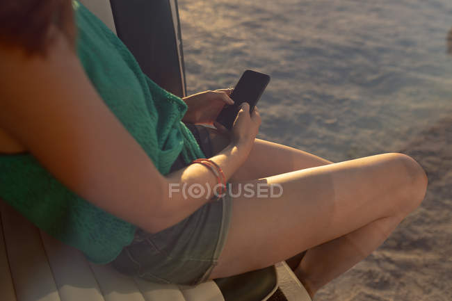 Parte centrale della donna utilizzando il telefono cellulare sul sedile anteriore del camper in spiaggia — Foto stock