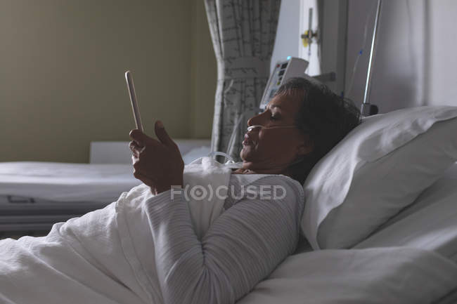 Side view of beautiful mature mixed-race female patient using digital tablet in the ward at hospital. — Stock Photo