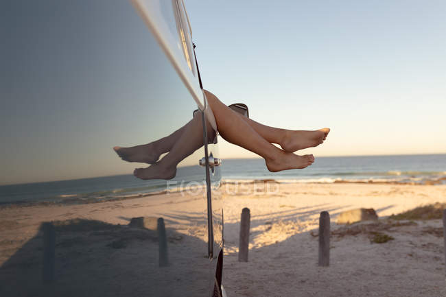 Baixa seção de mulher relaxante com os pés para cima em uma van campista na praia — Fotografia de Stock