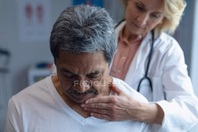 Вид на Кавказький жіночий лікар вивчення змішаної раси чоловічого пацієнта шиї в лікарні — стокове фото