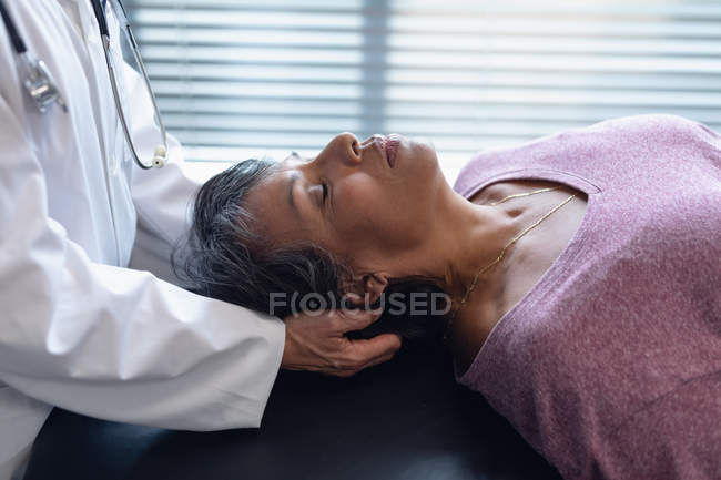 Visão lateral da médica examinando o pescoço mestiço de pacientes do sexo feminino no hospital — Fotografia de Stock