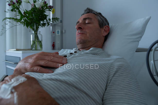 Front view of peaceful mature Caucasian male patient sleeping in bed with hand on his chest in the ward in hospital — Stock Photo