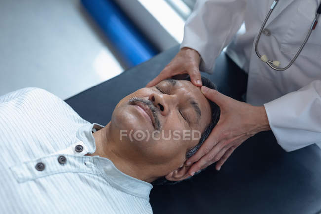Mid section of female doctor examining senior mixed-race male patient in hospital — Stock Photo