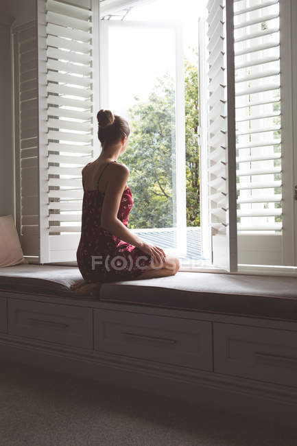 Вид сзади на кавказскую женщину, сидящую на сиденье окна в спальне дома — стоковое фото
