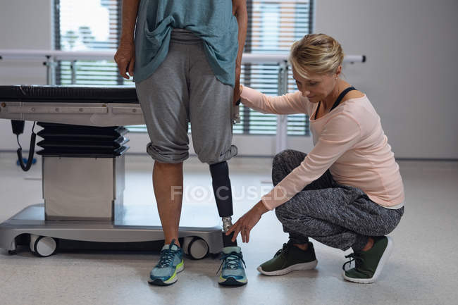 Vue de face du physiothérapeute féminin caucasien ajustant la jambe prothétique de la patiente à l'hôpital — Photo de stock