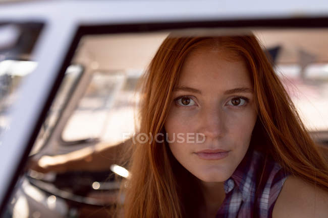 Cerrado de hermosa joven mujer caucásica mirando a la cámara en autocaravana en la playa - foto de stock