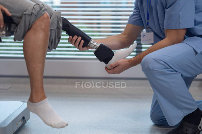 Sección baja del fisioterapeuta masculino ajustando la pierna protésica de la paciente femenina en el hospital - foto de stock