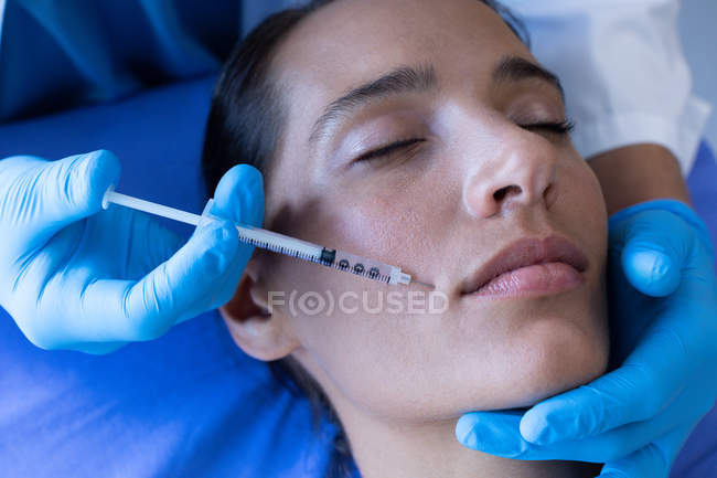 Close-up of surgeon giving injection to face of pretty Caucasian female patient at hospital — Stock Photo