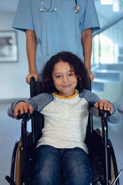Ritratto di ragazzo disabile di razza mista in sedia a rotelle con medico donna nel corridoio dell'ospedale — Foto stock