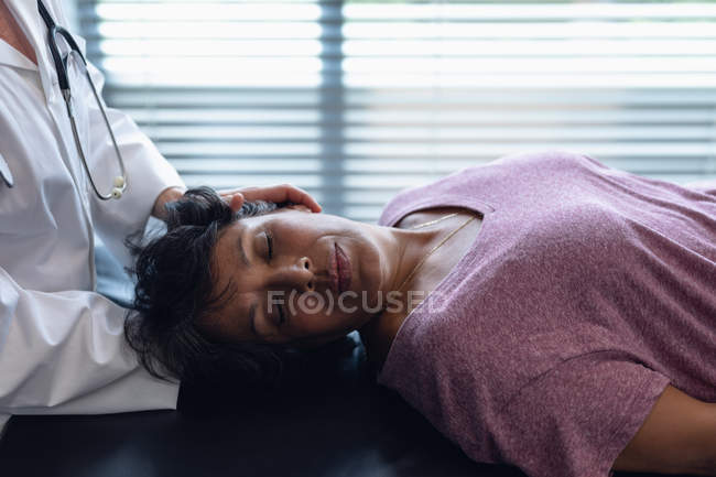 Вид спереду жіночого лікаря, який вивчає шию пацієнток змішаної раси в лікарні — стокове фото