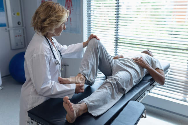 Vue latérale du médecin féminin caucasien examinant les patients masculins métis de retour à l'hôpital — Photo de stock