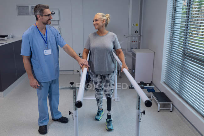 Vista frontal del fisioterapeuta masculino caucásico que ayuda al paciente a caminar con barras paralelas en el hospital - foto de stock