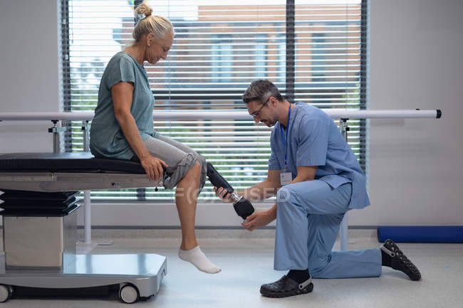 Seitenansicht des kaukasischen männlichen Physiotherapeuten, der die Beinprothese einer Patientin im Krankenhaus anpasst — Stockfoto