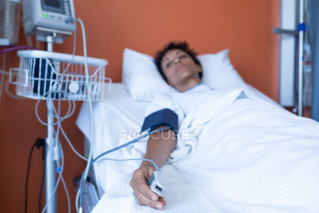 Vista frontale di paziente meticolosa di razza mista sdraiata a letto mentre l'ossimetria del polso misura la saturazione di ossigeno nel sangue in reparto in ospedale . — Foto stock