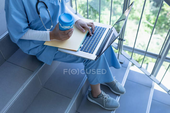 Low section of female doctor using laptop on staircase in hospital — Stock Photo