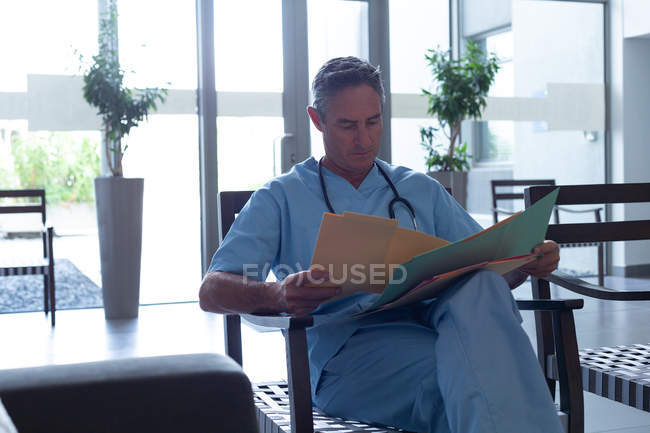 Vista frontal del guapo médico caucásico maduro que mira el informe médico en el vestíbulo en el hospital - foto de stock