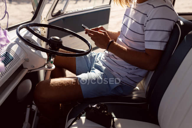 Sección media del joven usando teléfono móvil en furgoneta en la playa - foto de stock