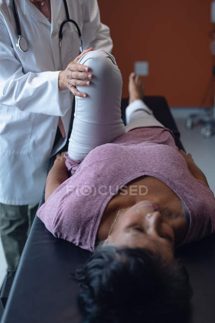 Vue de face du médecin féminin caucasien examinant la jambe des patientes métisses à l'hôpital — Photo de stock