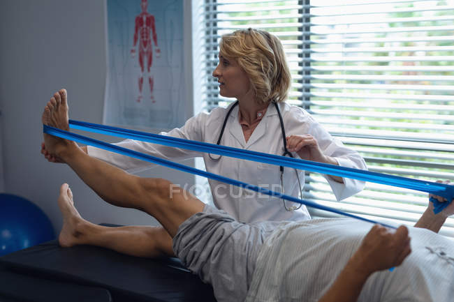 Seitenansicht einer kaukasischen Ärztin bei der Untersuchung eines Patientenbeins mit Resistenzband im Krankenhaus — Stockfoto
