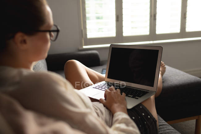 Vista lateral da mulher caucasiana usando laptop em um sofá na sala de estar em casa — Fotografia de Stock