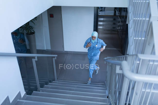 Vue de face de la jeune femme médecin métis dans le hijab courant à l'étage à l'hôpital — Photo de stock