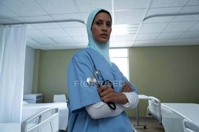 Retrato de bela mestiça médica feminina em hijab de pé com os braços cruzados e estetoscópio na mão no hospital — Fotografia de Stock