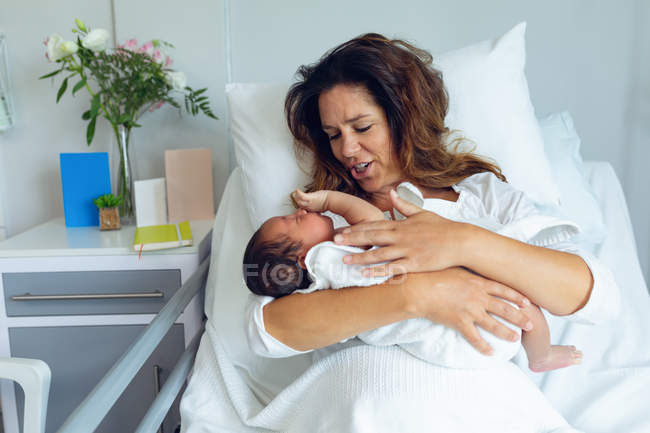 Вид спереду красива мати тримає свою новонароджену дитину після праці в палаті в лікарні — стокове фото