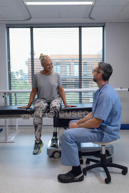Vue latérale du kinésithérapeute masculin caucasien heureux parlant avec une patiente handicapée à l'hôpital — Photo de stock