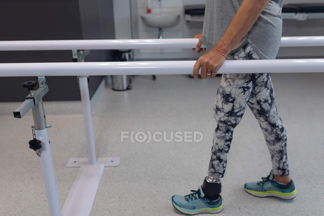 Low section of female amputee patient walking with parallel bars in hospital — Stock Photo