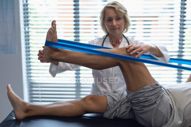 Front view of Caucasian female doctor examining patient leg with resistance band in hospital — Stock Photo