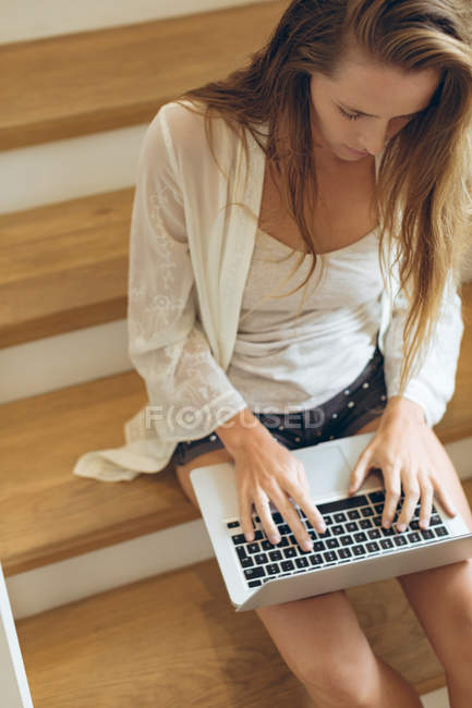 Vue haute de belle femme caucasienne en utilisant un ordinateur portable sur les escaliers à la maison — Photo de stock