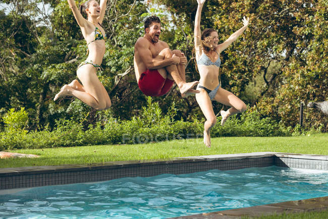Vista frontal de amigos caucasianos felizes do sexo masculino e feminino pulando na piscina no quintal — Fotografia de Stock