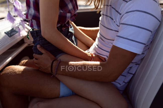 Mid section of woman sitting on man's lap in front seat of camper van at beach — Stock Photo