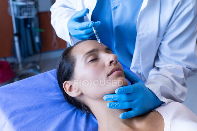 Mittelteil eines männlichen Chirurgen, der einer hübschen kaukasischen Patientin im Krankenhaus eine Injektion ins Gesicht verabreicht — Stockfoto