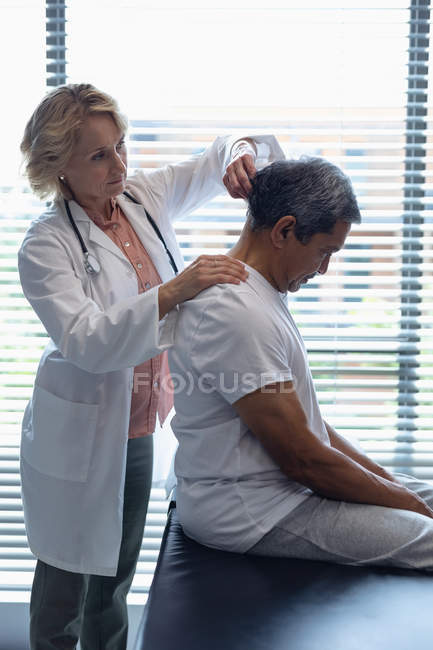 Vista lateral del médico femenino caucásico examinando el cuello del paciente masculino de raza mixta senior en el hospital - foto de stock