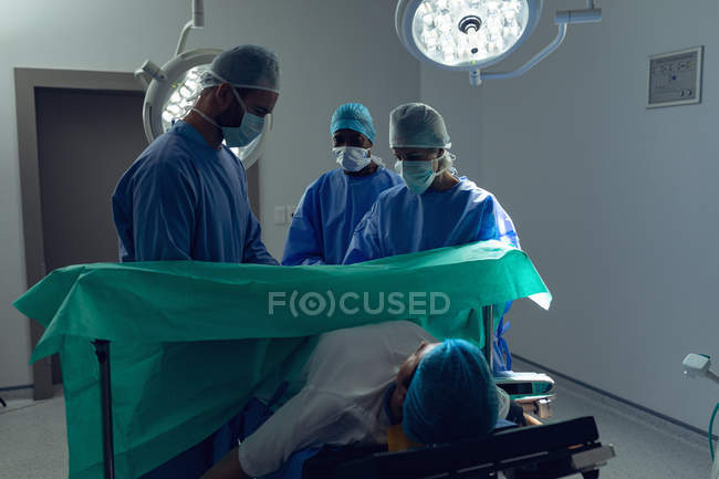 Visão frontal da equipe médica diversa examinando a gestante durante o parto no teatro de operação no hospital — Fotografia de Stock
